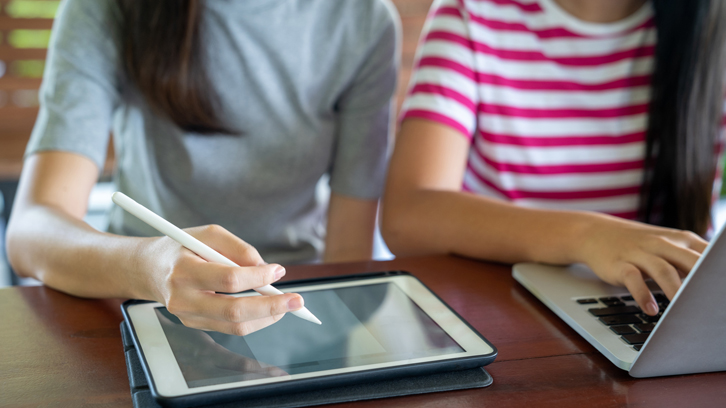 dues estudiants treballant amb una tablet i un portàtil. Només se'ls hi veuen les mans
