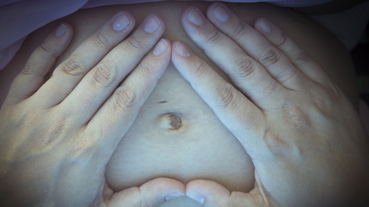 Mans dibuixant un cor en la panxa d'una dona