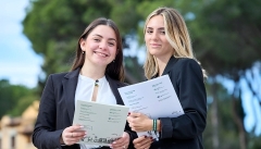 Dues estudiants somriuen i porten carpetes dels estudis