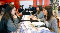 Una estudiant xerra amb una dona jove que li mostra fulletons informatius