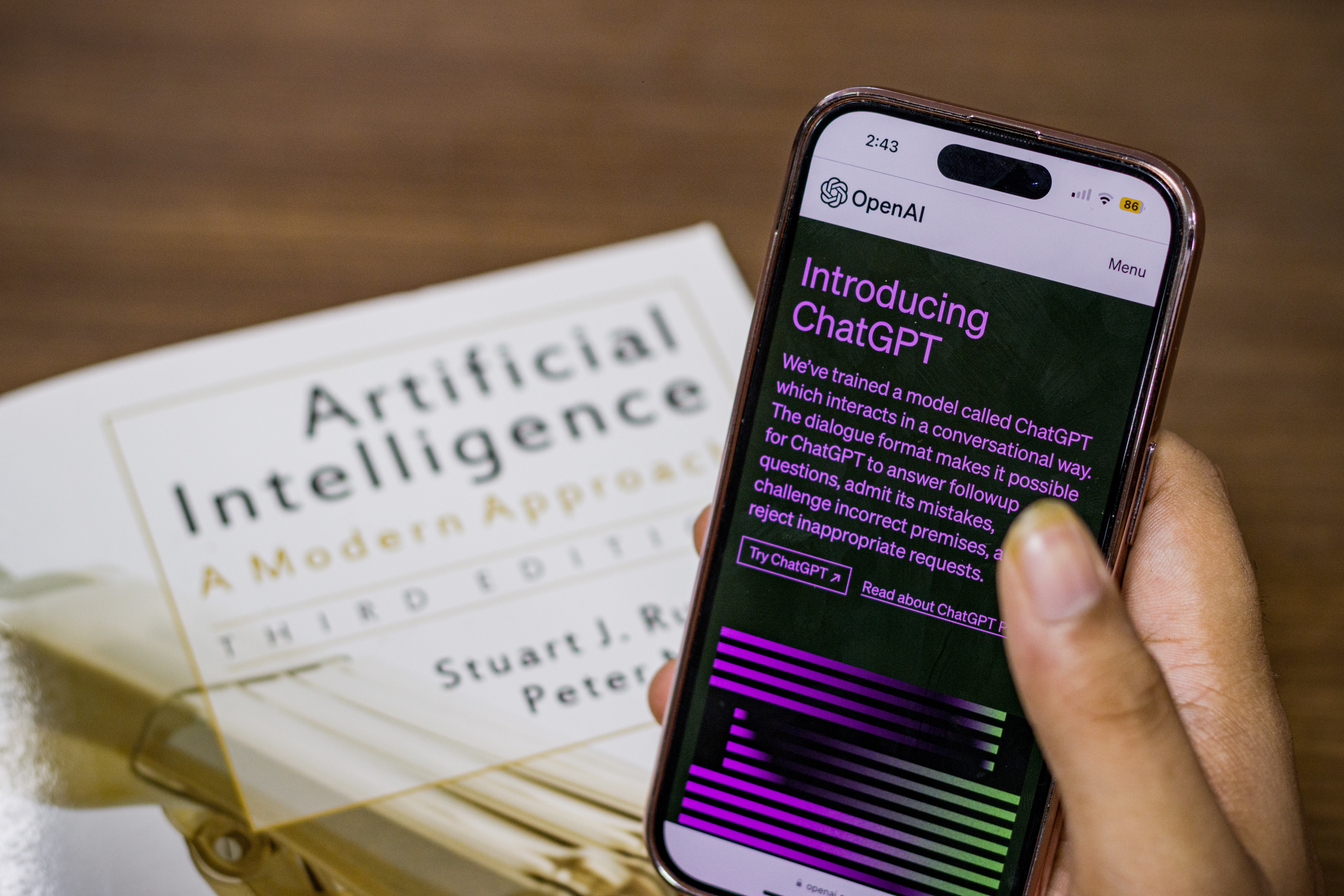 Pantalla de mòbil amb informació del ChatGPT i un llibre d'intel·ligència artificial de fons