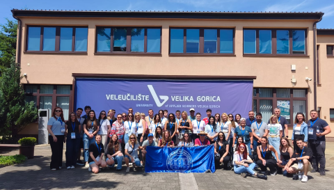 Un grup de persones posa amb una bandera blava de la universitat Velika davant d'un edifici