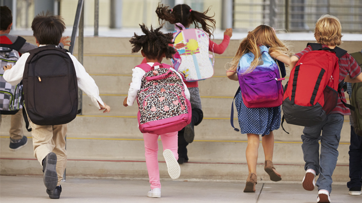 nens de primària d'esquenes corrents cap a l'entrada de l'escola