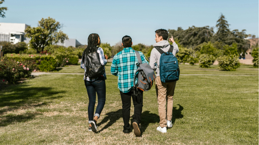 Tres estudiants caminant per la gespa del campus