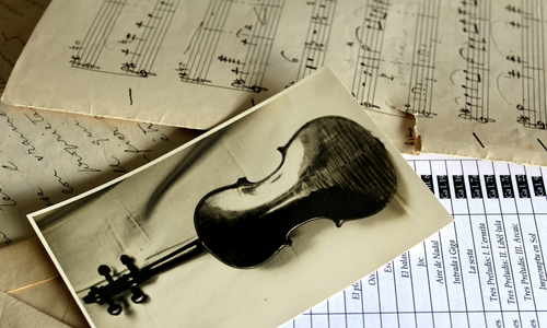 Fotografia d'un violí en blanc i negre sobre partitures manuscrites i documents d'arxiu relacionats amb el fons Joan Massià i Prats.