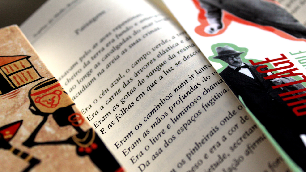 Primer pla d’un llibre obert en portuguès, amb text imprès a les pàgines, envoltat d’altres llibres il·lustrats de la col·lecció del Premi de Traducció Giovanni Pontiero.