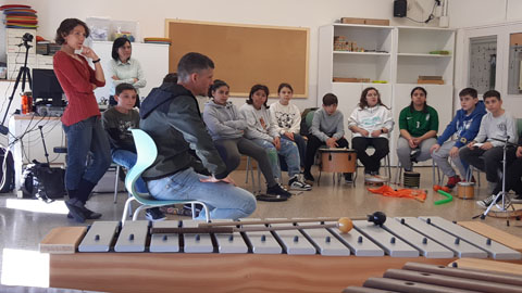  Aula amb alumnes asseguts en cercle participant en una activitat musical amb instruments de percussió, com un xilòfon, guiats per un docent en un context educatiu.