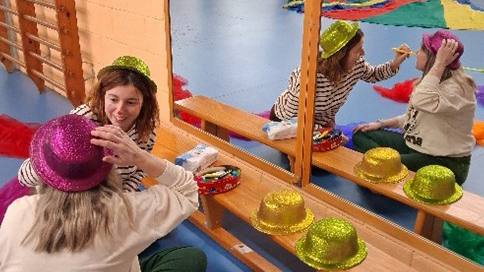Dos infants jugant davant d’un mirall, provant-se barrets de colors en un espai de psicomotricitat o joc simbòlic.