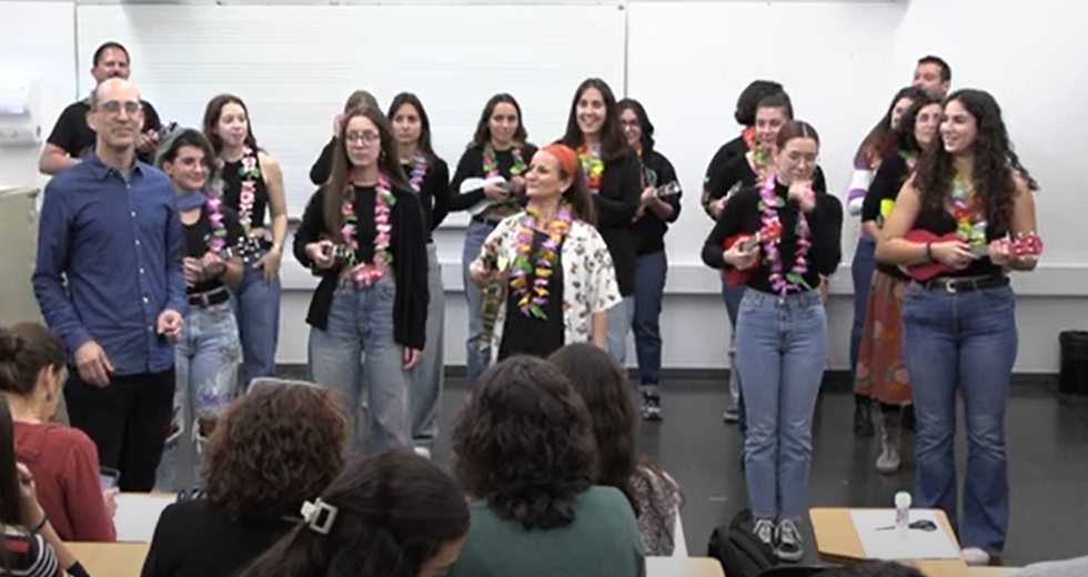  Els participants al concert cantant i tocant ukeleles en una aula, amb ambient festiu i elements com collars de flors, en una activitat musical col·lectiva.