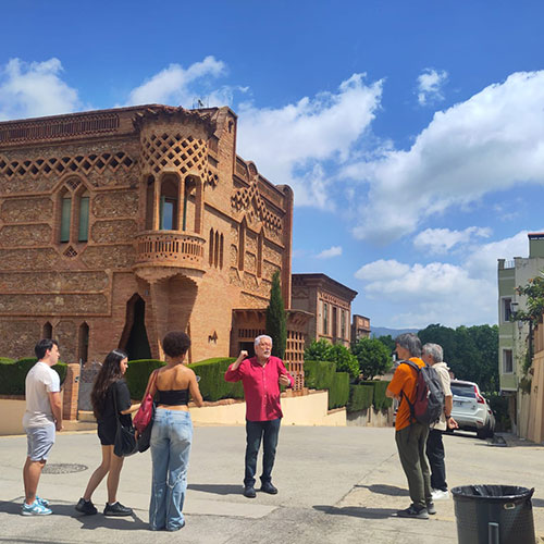 Amplia la imatge Grup de persones escoltant una explicació davant d'un edifici modernista