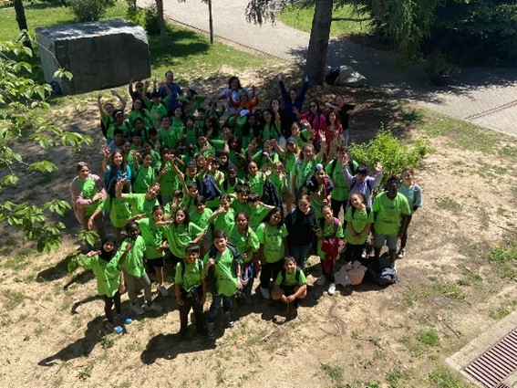  Grupo numeroso de niños y niñas del programa CROMA con camisetas verdes posando juntos al aire libre, mirando hacia arriba y saludando con las manos.