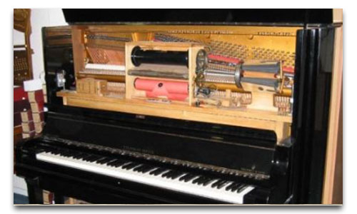 La imagen muestra el interior de un piano de rollos, donde se pueden ver los rollos de papel perforado y el sistema de engranajes que permite que el piano reproduzca música de forma automática.