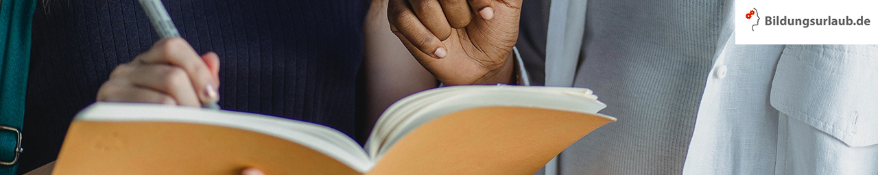  Image of two people holding a yellow book while writing with a pen