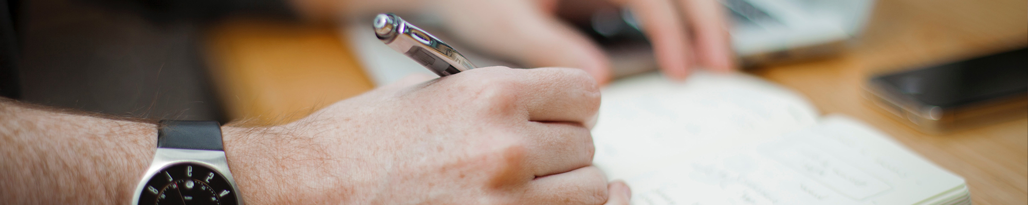 Image of a person writing in a notepad with a pen