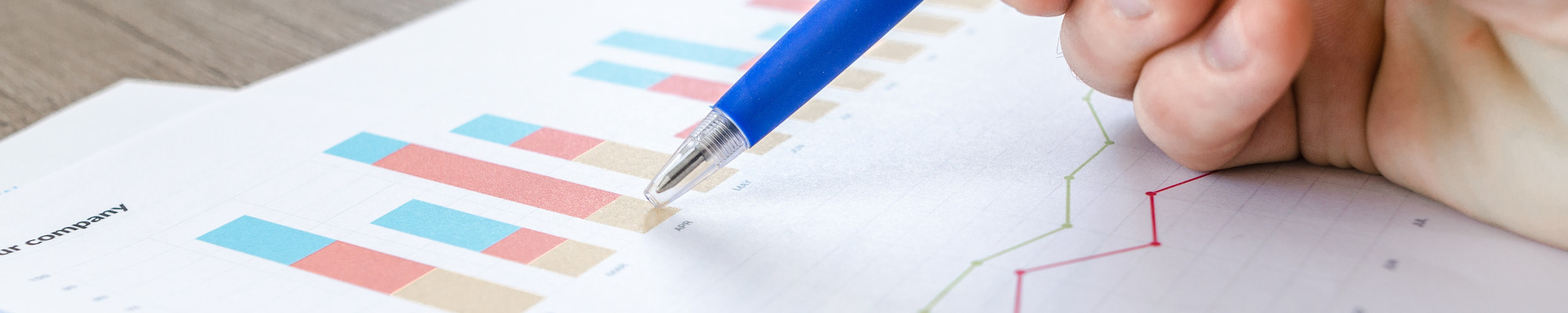 Image of a person holding a pen, pointing at a paper containing bar and line charts